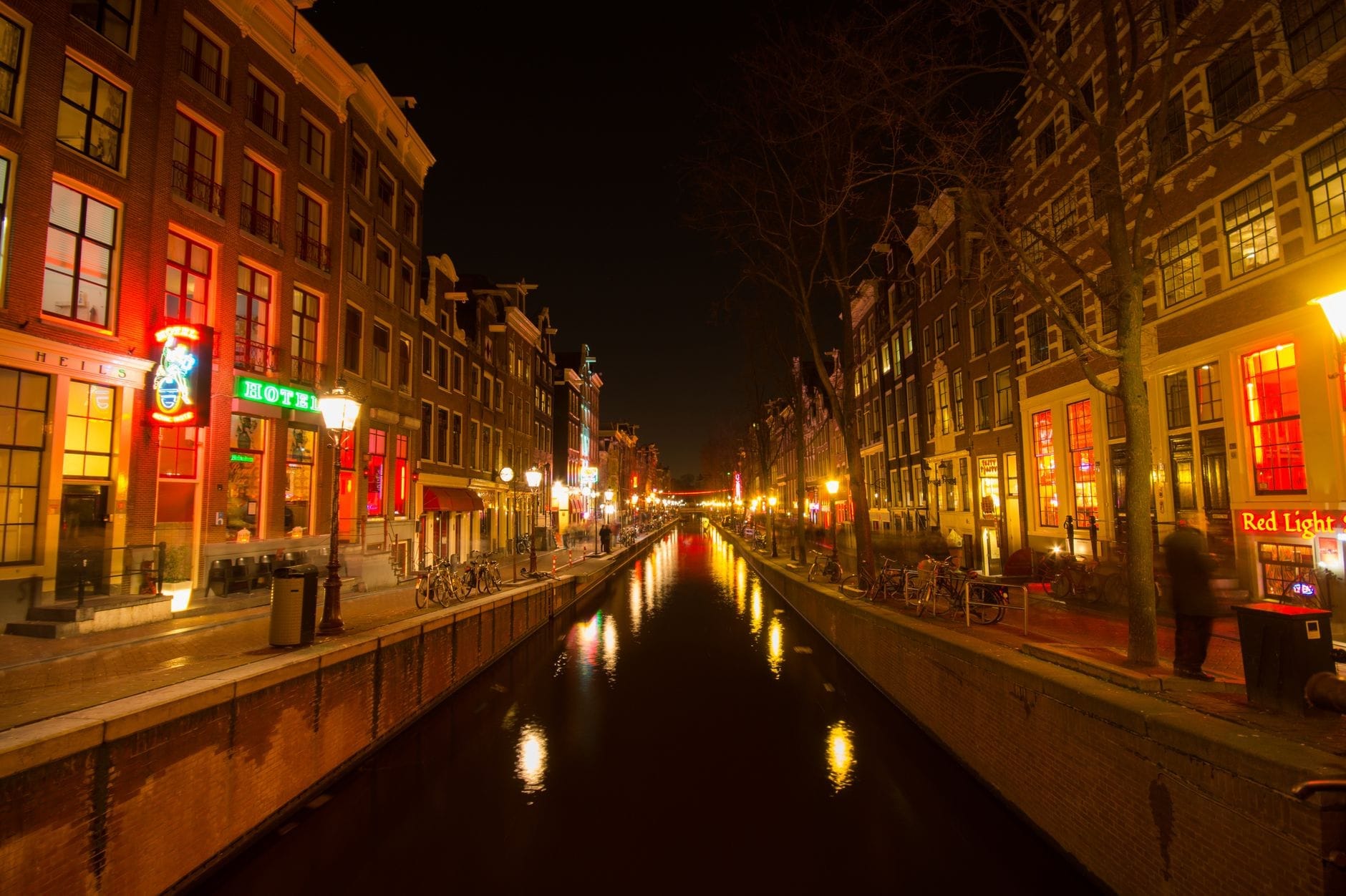 Canal de Ámsterdam de noche con bares iluminados de neón, hoteles y carteles del Barrio Rojo, mostrando el vibrante ambiente nocturno.