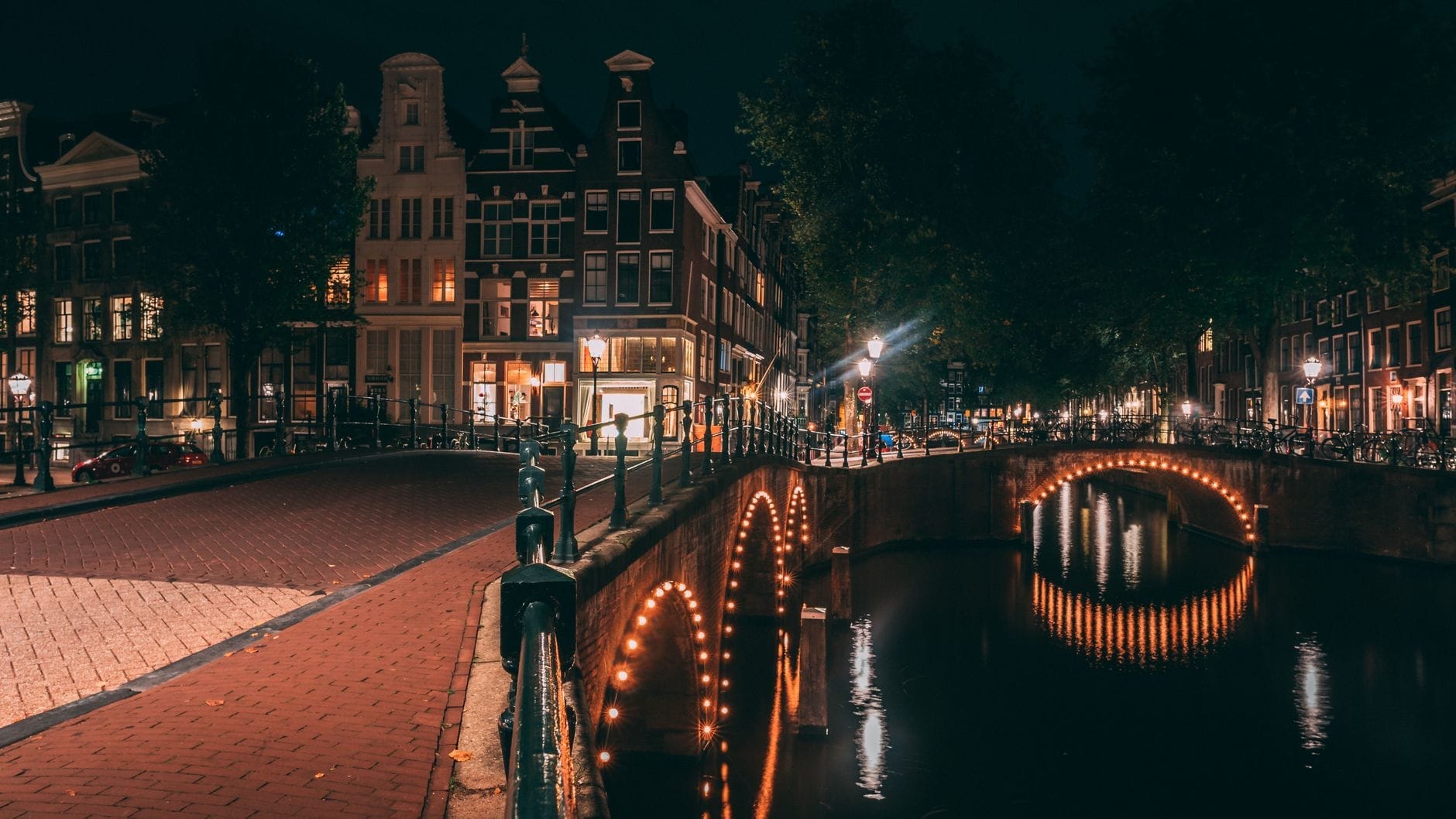 Vista nocturna de un canal de Ámsterdam iluminado con sus icónicos puentes y edificios históricos, reflejo de la vibrante vida nocturna de la ciudad.