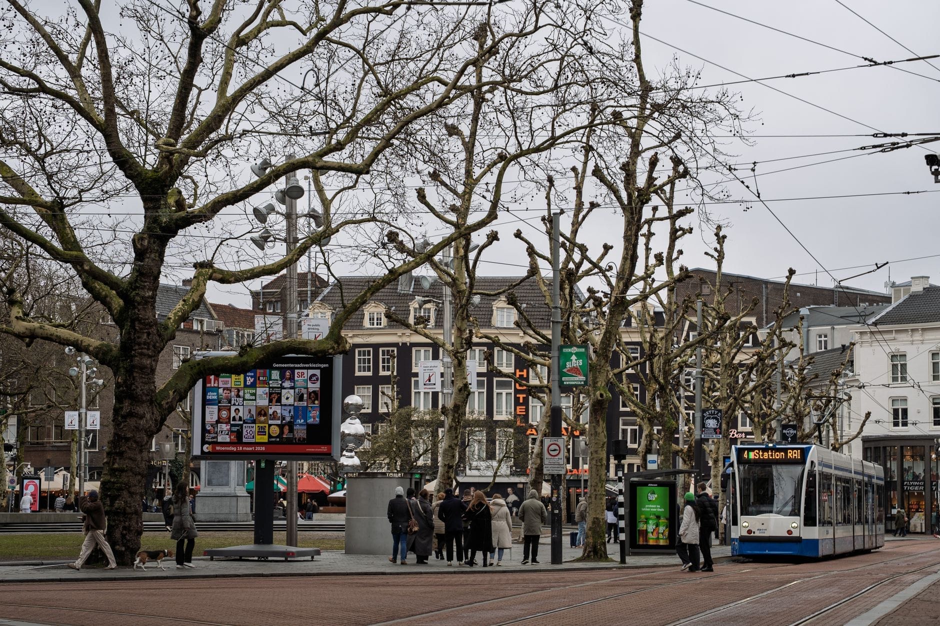 Tranvía de Amsterdam en una parada urbana con personas esperando y máquinas expendedoras de billetes cercanas, mostrando el transporte público en un entorno urbano real.
