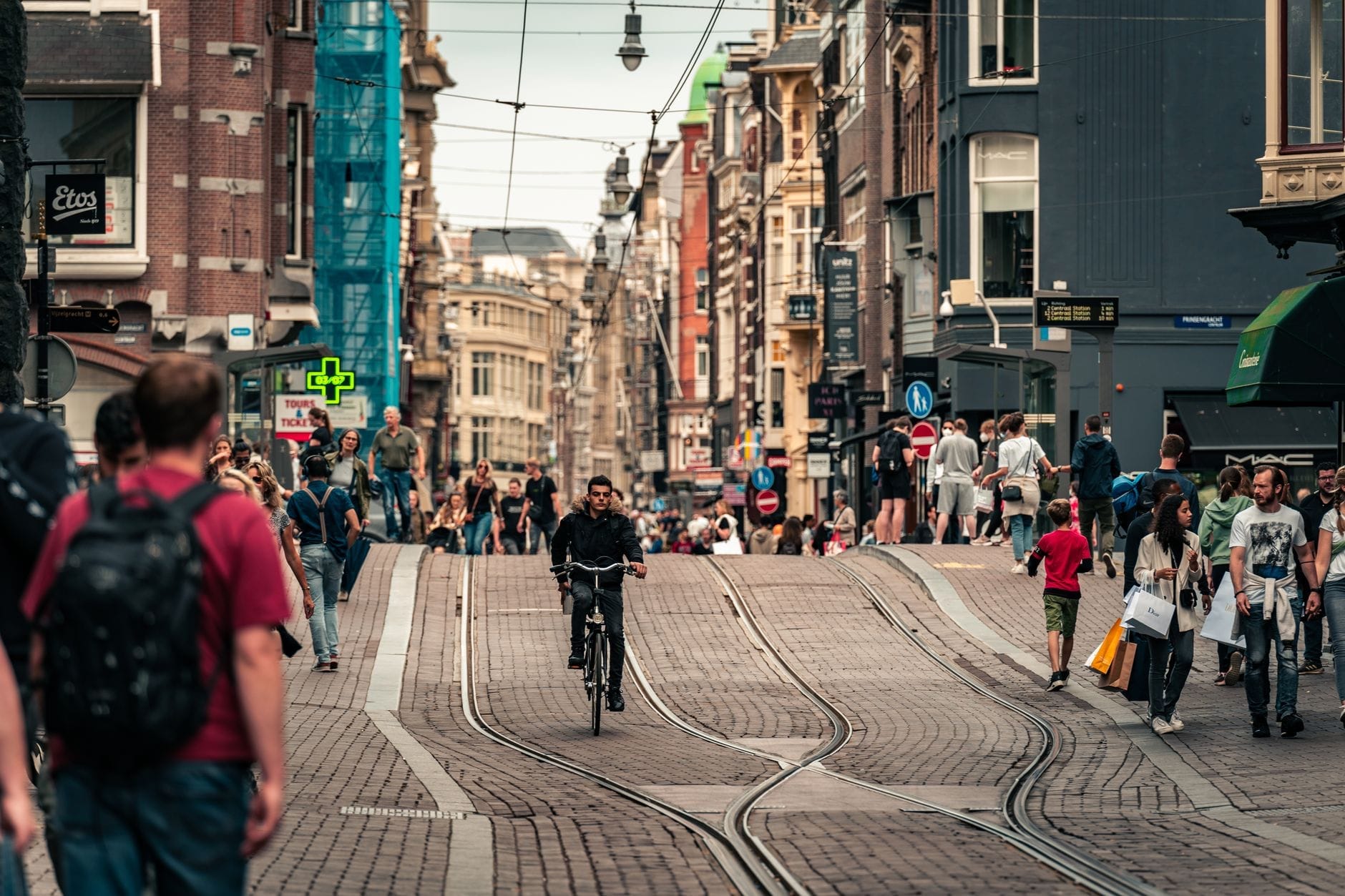 Calle concurrida de Ámsterdam con ciclistas entre peatones, raíles de tranvía y edificios históricos, que reflejan la animada vida urbana y la icónica cultura de la bicicleta.