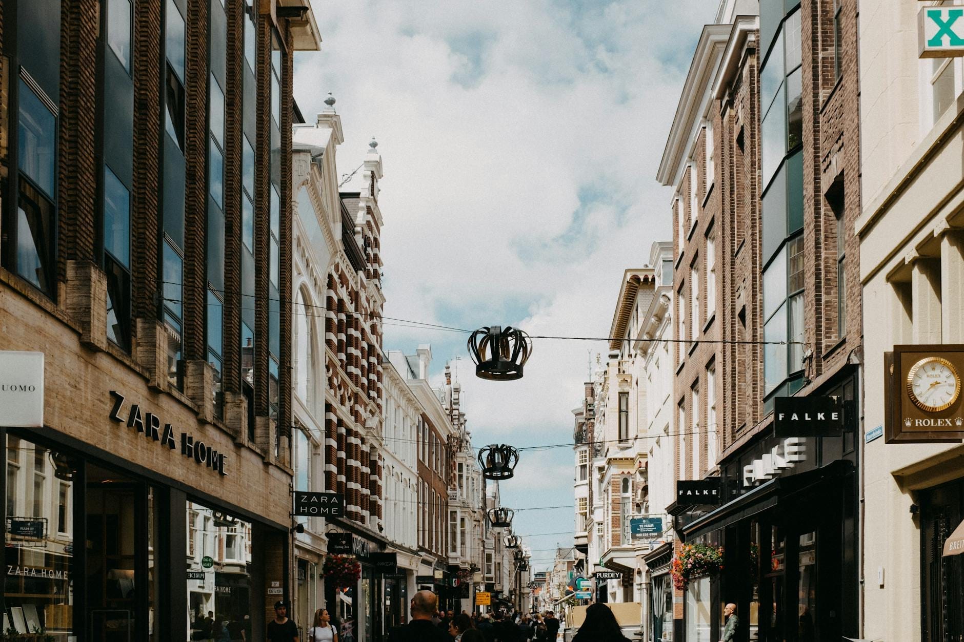 Concurrida calle comercial de Ámsterdam flanqueada por boutiques y peatones que pasean bajo un cielo azul con algunas nubes.