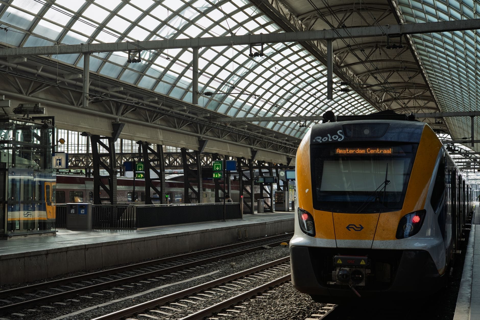 Tren moderno en un andén dentro de la estación Amsterdam Centraal, bajo un techo arqueado de cristal con señalización visible.