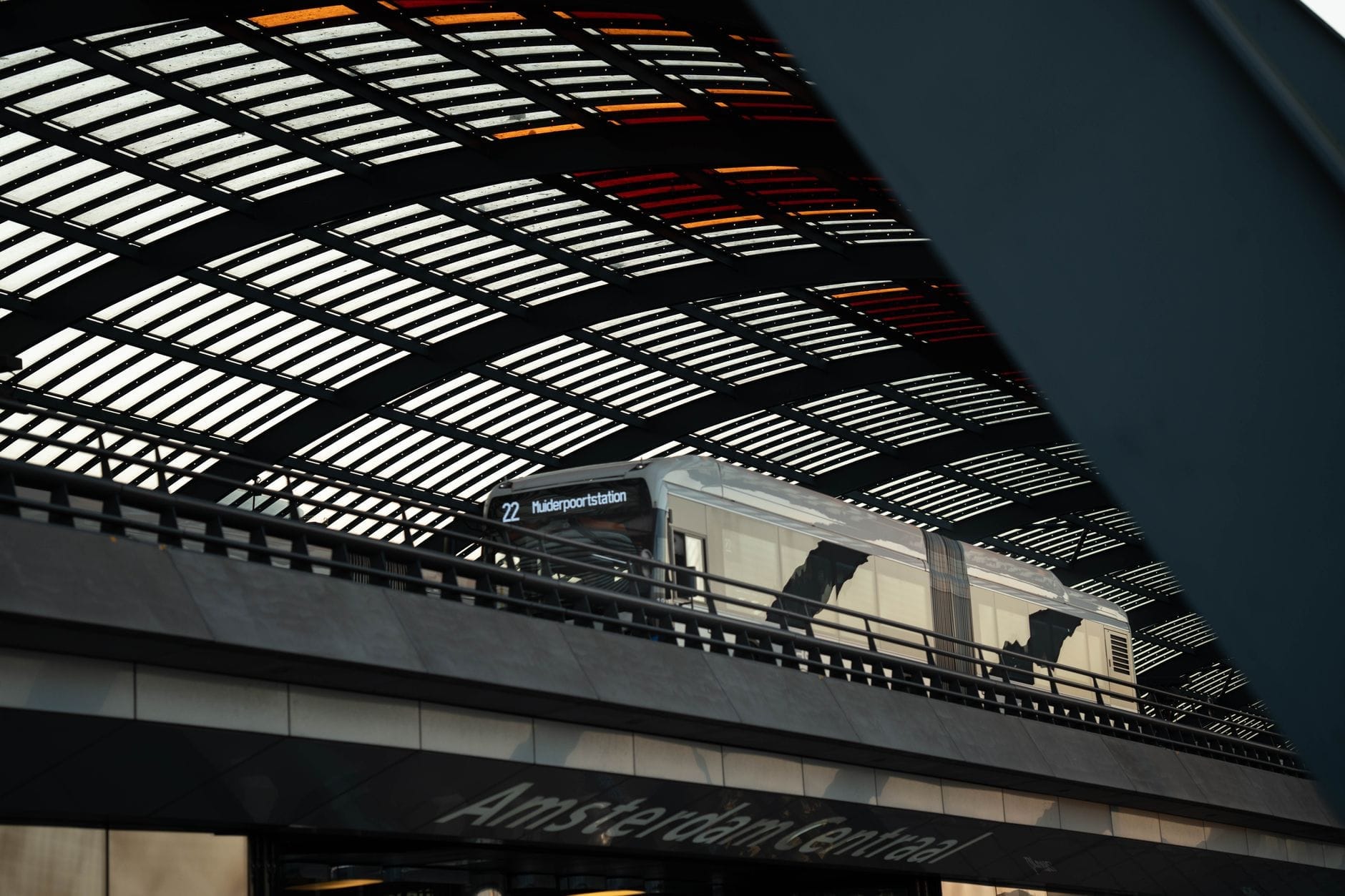 Andén cubierto en la estación Amsterdam Centraal con un tren a lo lejos y un letrero visible bajo el techo de cristal y acero.