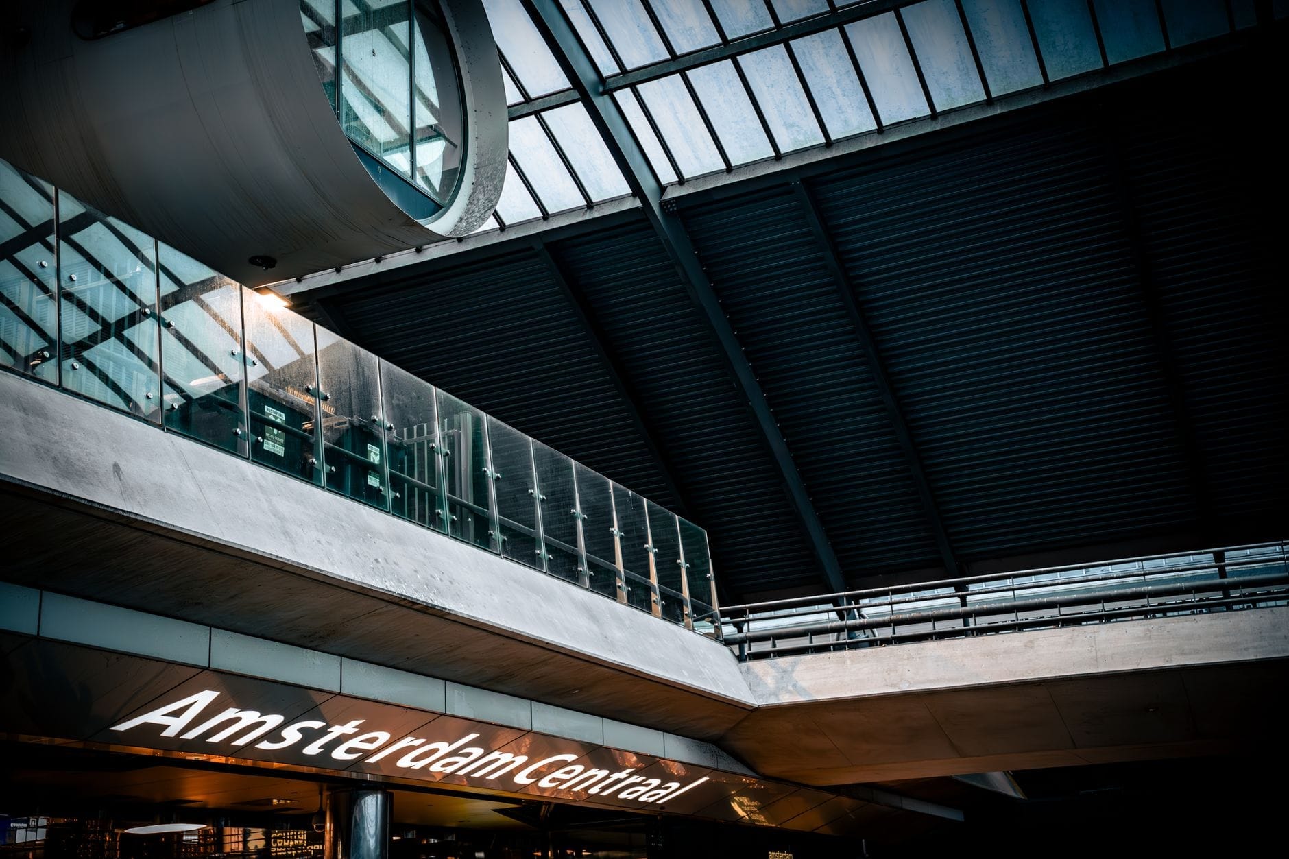 Techo de cristal moderno y señalización interior de la estación de ferrocarril Amsterdam Centraal, con parte del nombre de la estación visible y buena iluminación.