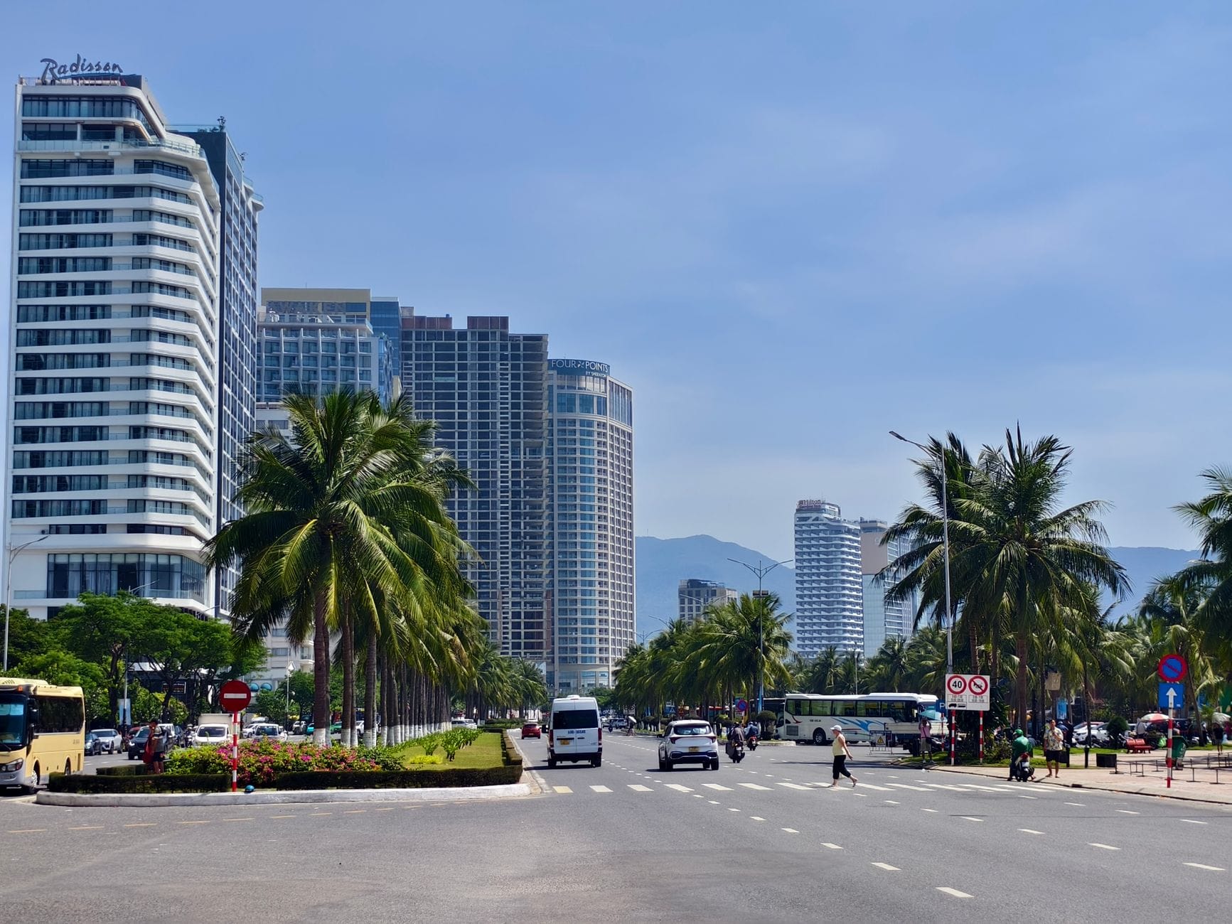 ถนนสายกว้างในย่านอันเถืองริมทะเลของดานัง มีต้นปาล์ม โรงแรมและการจราจรใต้ท้องฟ้าสีฟ้าใสกลางวัน