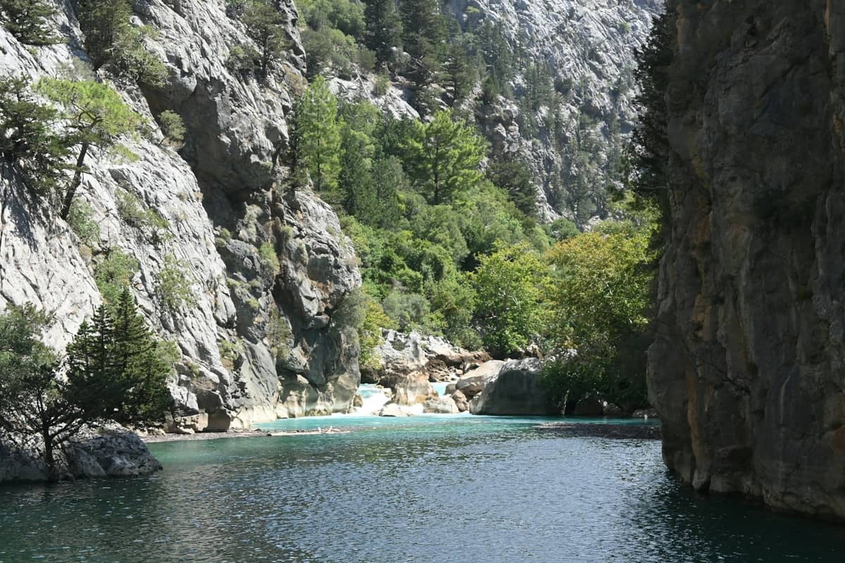 Clear turquoise river running through steep rocky canyon with lush green trees under sunlight near Antalya.