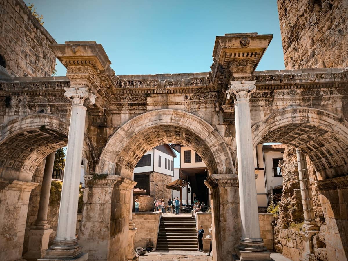 Imposing Roman stone arch with white marble columns and vaulted ceiling, surrounded by old town buildings in Antalya under a blue sky.