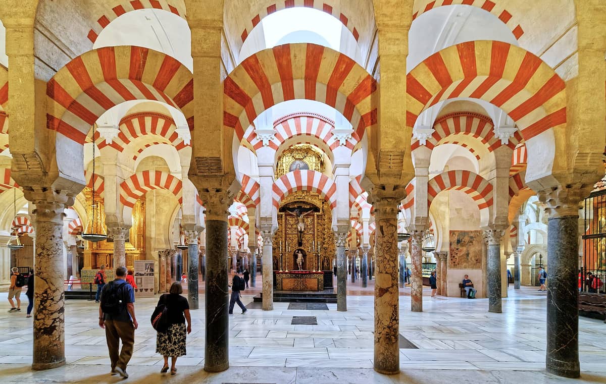 มุมมองกว้างของภายใน Mezquita-Catedral de Córdoba พร้อมซุ้มโค้งลายแถบสีแดงและสีขาวอันโด่งดังและนักท่องเที่ยวที่กำลังสำรวจ