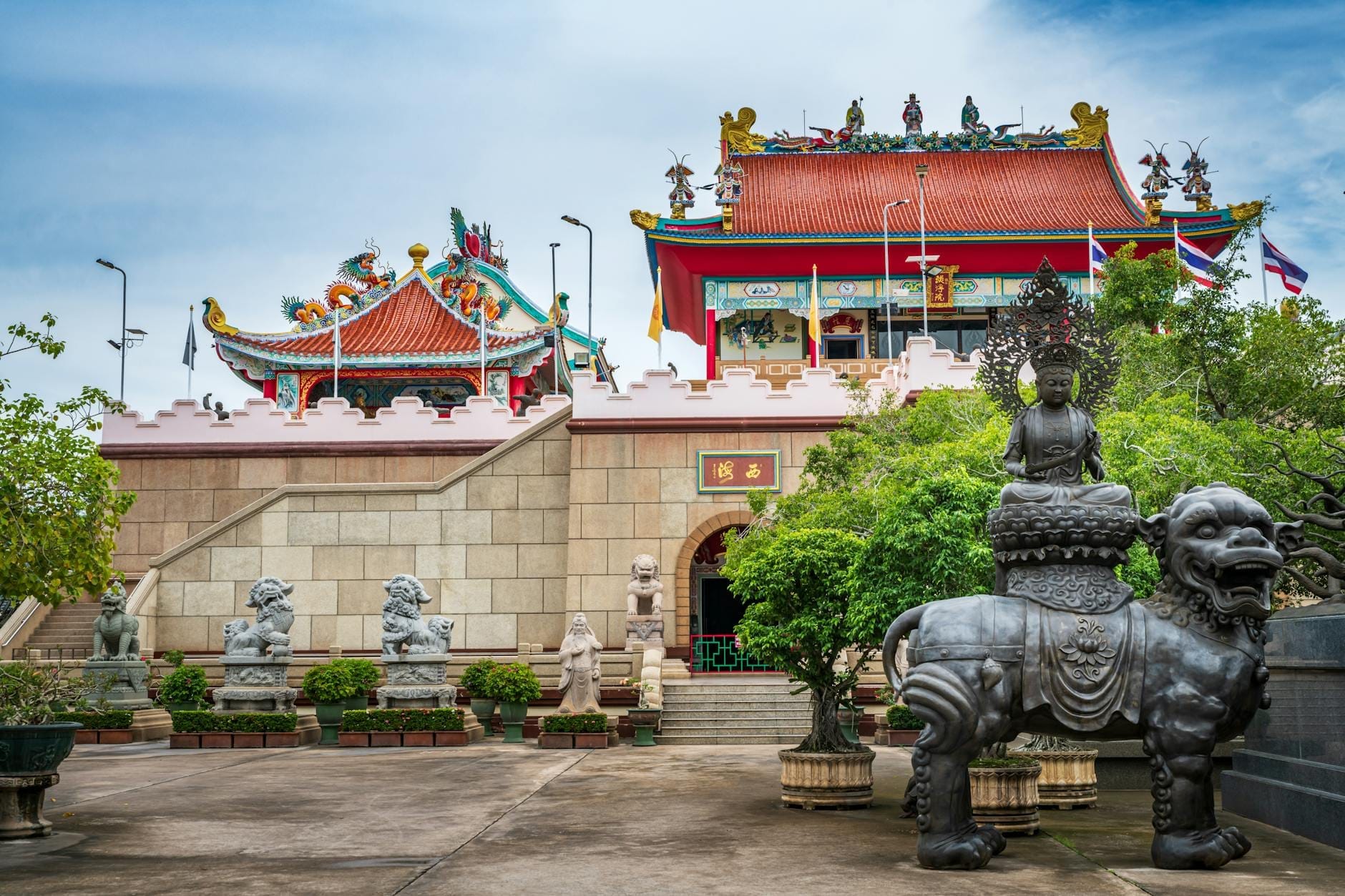 Cortile d'ingresso dell'Anek Kusala Sala con statue cinesi, elaborate sculture e colorati edifici templari sotto un cielo luminoso a Pattaya, Thailandia.
