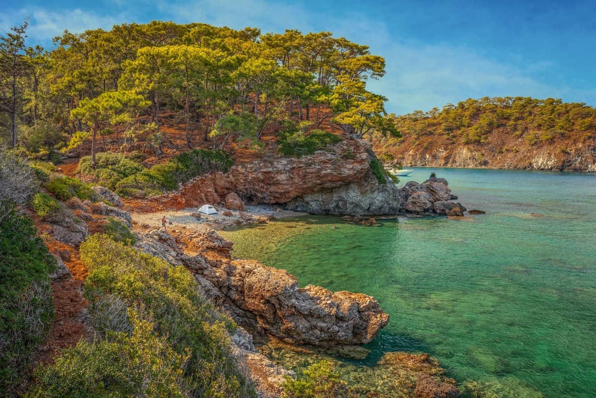 Rocky, tree-covered coastline and a small secluded beach with clear turquoise water west of Antalya, Turkey.