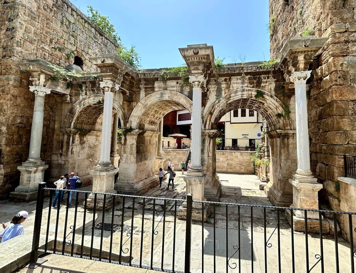 Stone arches and columns of Hadrian's Gate, with people walking beneath the ancient structure in central Antalya.