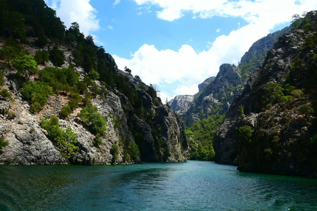 Clear turquoise river winding through dramatic rocky canyon with lush green trees under a bright blue sky in Antalya’s wilderness.