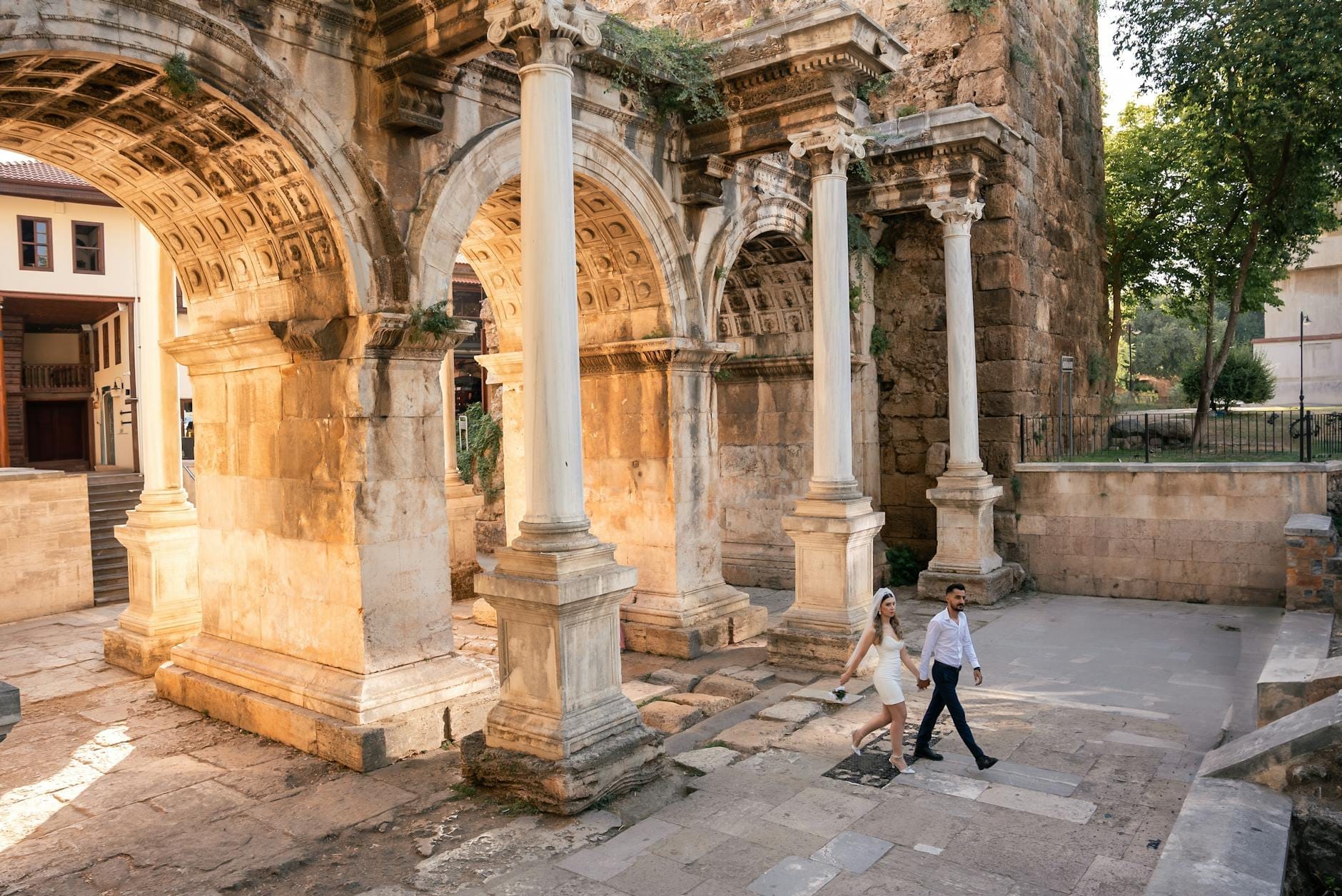 Um casal caminha de mãos dadas sob os antigos arcos de mármore do Portão de Adriano na histórica cidade velha de Antalya, Kaleiçi.