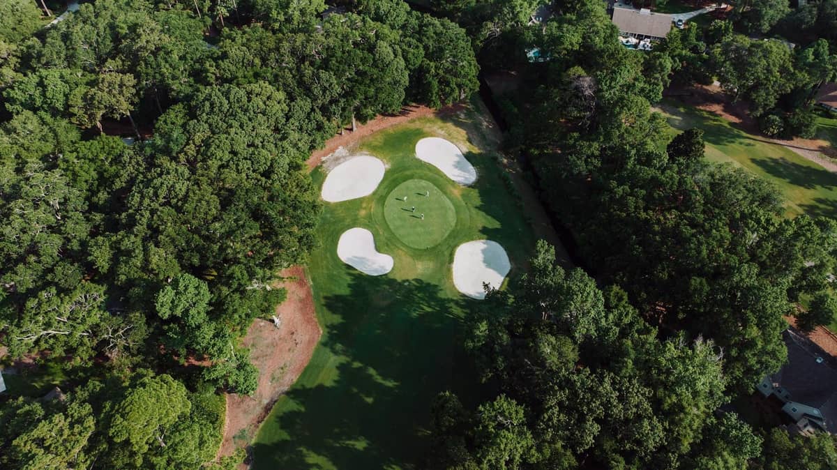 Aerial view of a green golf course surrounded by trees with visible sand bunkers and manicured fairways.
