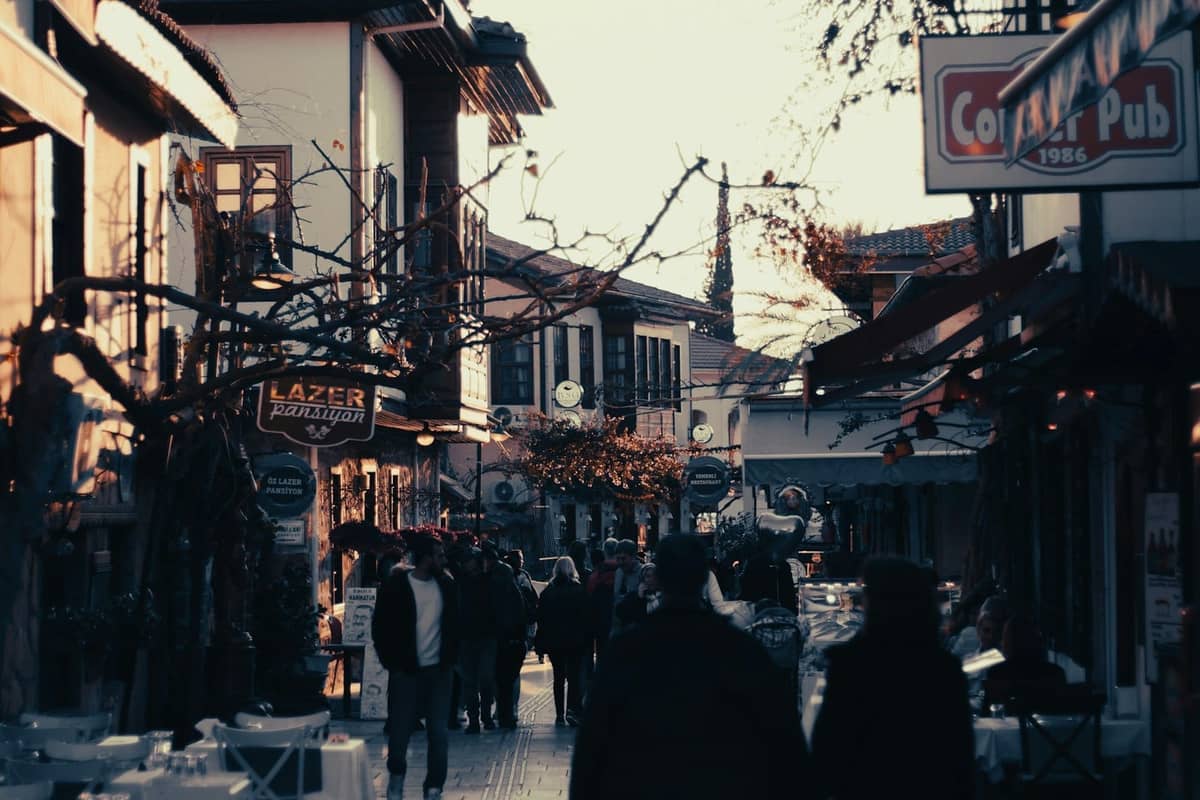 Old town street in Antalya filled with people, bars, cafes, and signs in the early evening light.