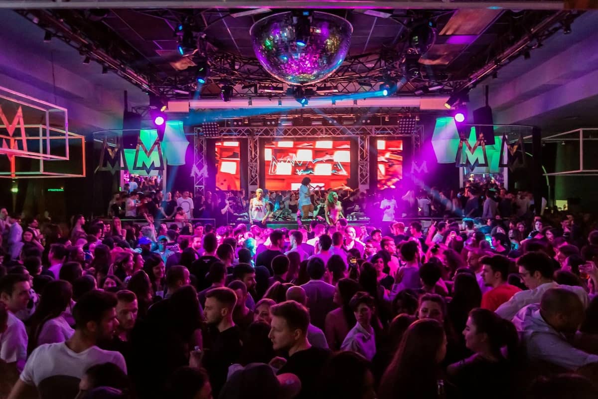 Packed nightclub in Antalya with colorful lights, DJ on stage, and large crowd dancing under disco ball.