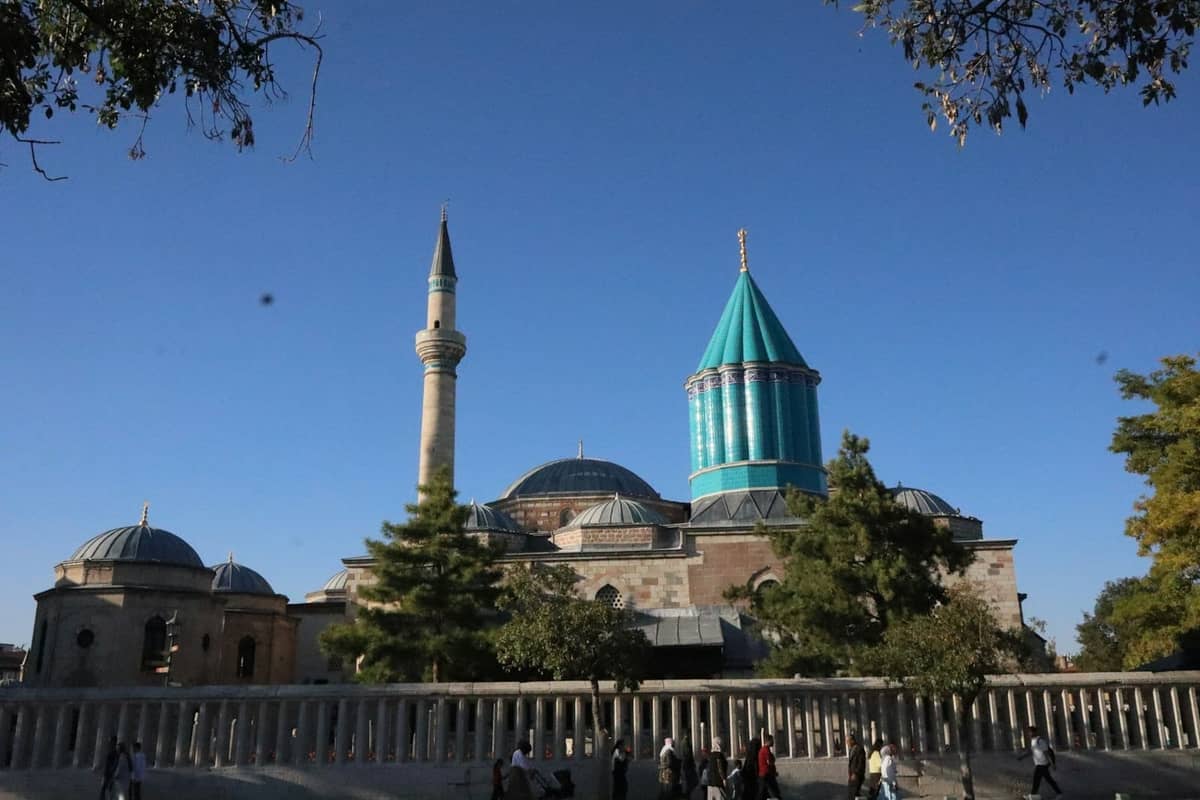 A clear view of the Mevlana Museum and its iconic turquoise dome in Konya under a bright blue sky.