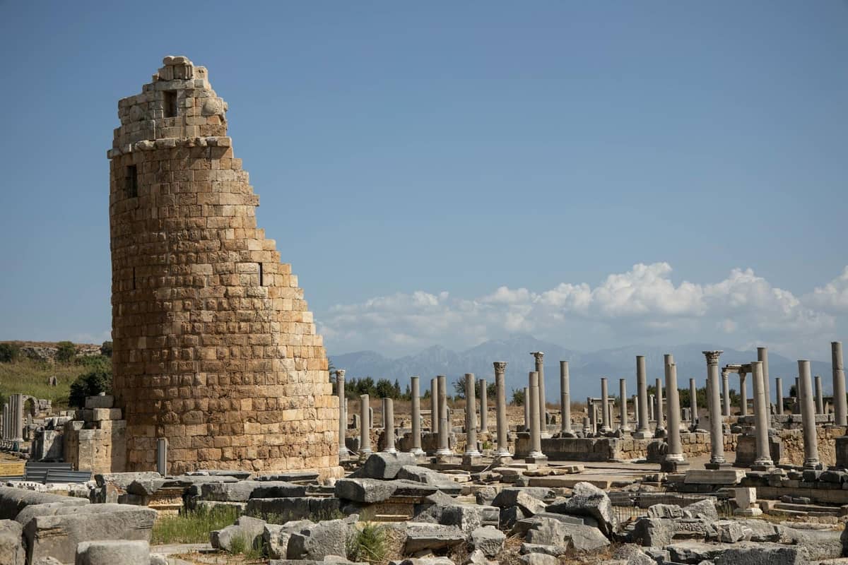 Ancient stone tower and colonnade ruins under blue sky at a historical site near Antalya.