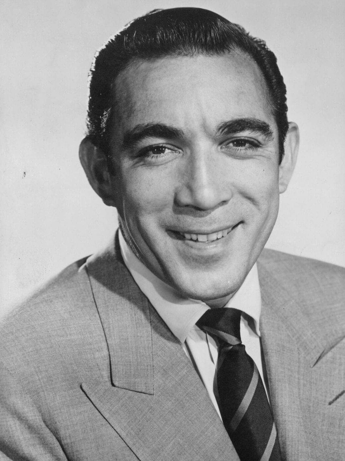 Black and white portrait of a man in a light suit and striped tie, smiling at the camera against a plain background.