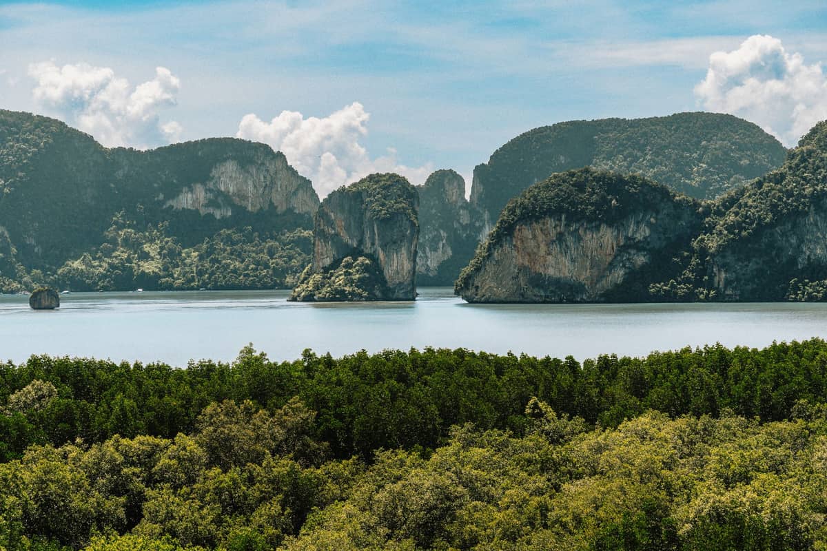 Blick über die Bucht Ao Tha Lane in Krabi, Thailand – dichter Mangrovenwald trifft auf dramatische Kalksteinkarstfelsen unter einem teils bewölkten blauen Himmel.