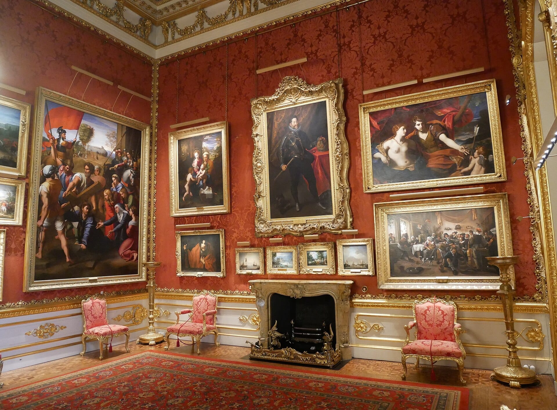 Opulenta galleria d'arte ad Apsley House con dipinti con cornici dorate, carta da parati rossa con motivi, camino ornato e sedie antiche tappezzate in rosa.