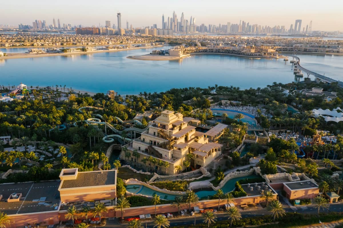 Luftaufnahme des Aquaventure Waterparks im Atlantis, The Palm in Dubai mit Wasserrutschen, Pools und der Palm Jumeirah sowie der Skyline von Dubai im Hintergrund.
