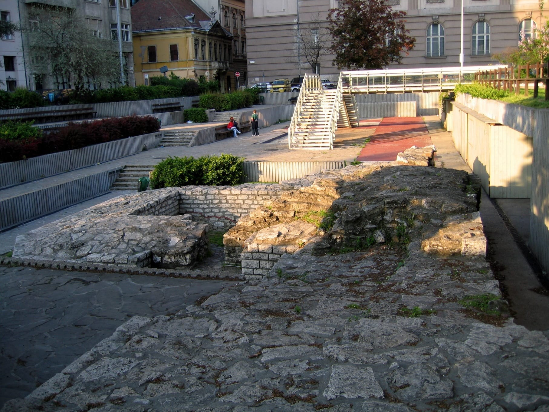 Mga sinaunang guho ng bato ng Aquincum Museum & Roman Ruins sa Budapest, napapalibutan ng mga modernong gusali at mga hardin sa malambot na liwanag ng hapon.