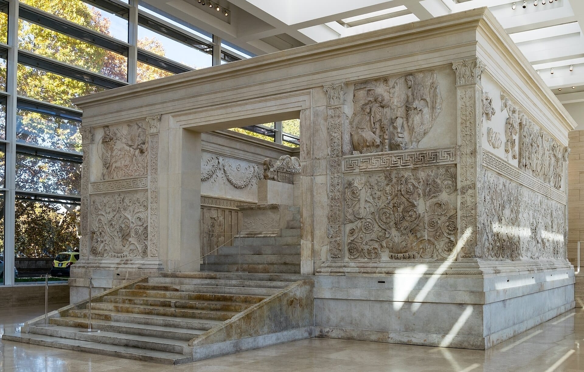 The Ara Pacis Augustae in Rome, showing intricate marble reliefs and a broad staircase inside a bright, modern glass pavilion.
