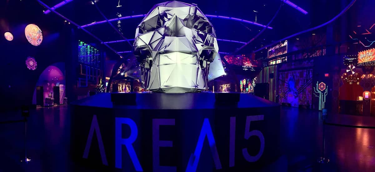 Patung tengkorak geometris besar di jantung AREA15 Las Vegas, dikelilingi lampu neon dan instalasi seni mural yang penuh warna.