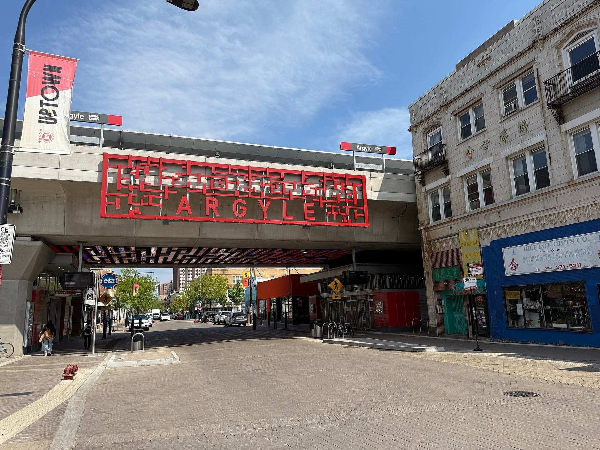 Vista a livello stradale del viadotto di Argyle Street e dei negozi circostanti nell'Uptown di Chicago, con insegne colorate e cielo azzurro limpido.