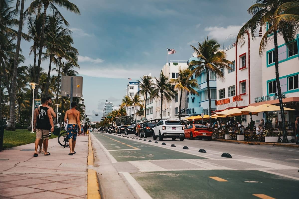 View down Ocean Drive in Miami Beach with art deco hotels, palm trees, sidewalk cafes, pedestrians, and moody afternoon light.