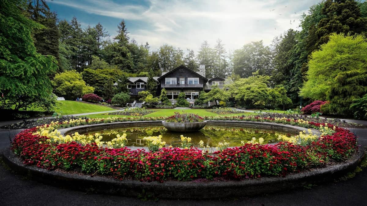 Ein gepflegter kreisförmiger Blumengarten mit einem Brunnen vor einem Gebäude im Heritage-Stil, umgeben von üppigem Grün in Vancouver.