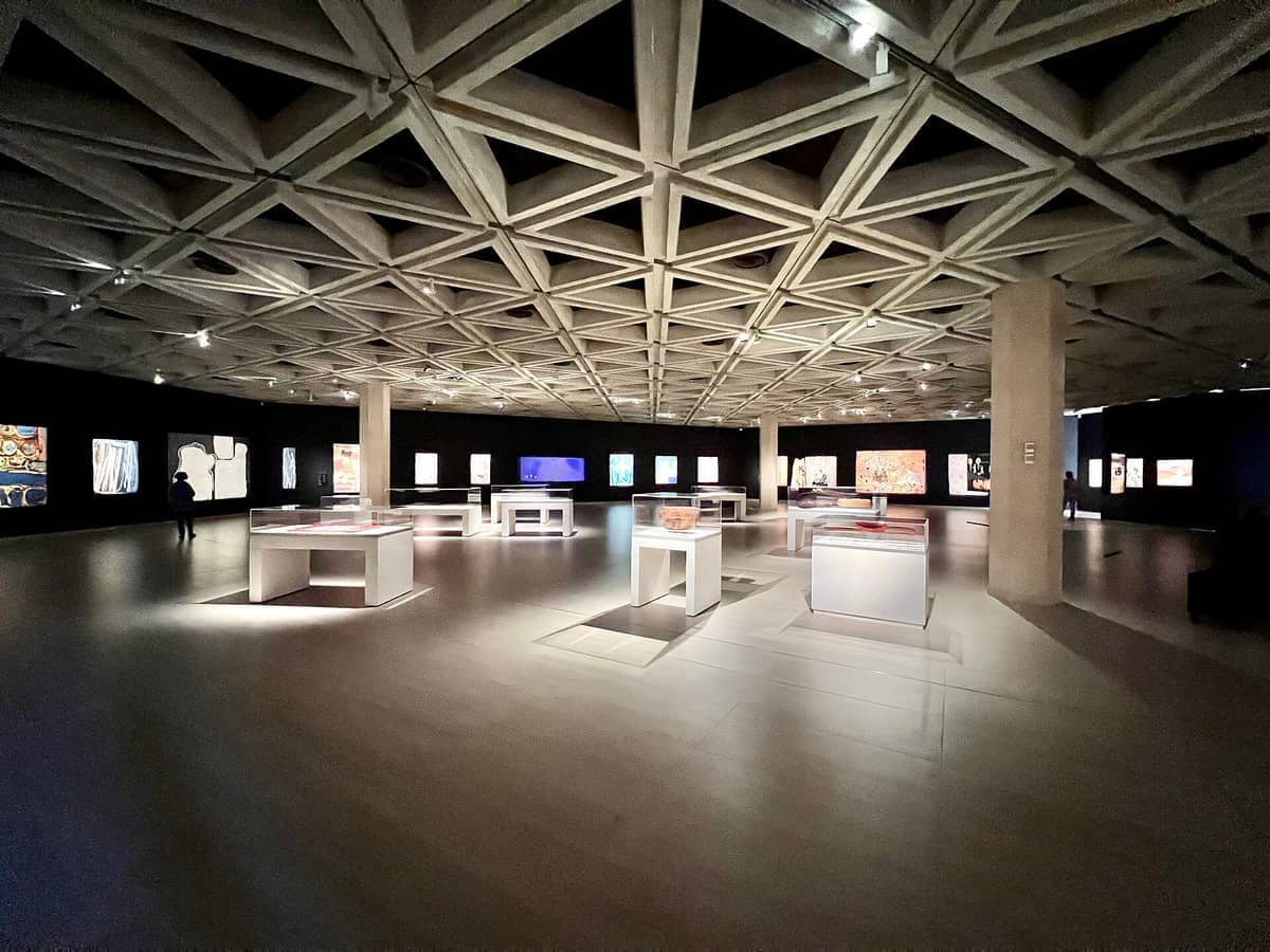 Amplio interior de galería en la Art Gallery of Western Australia, con techo geométrico, exhibiciones de arte iluminadas y esculturas bajo suaves focos.