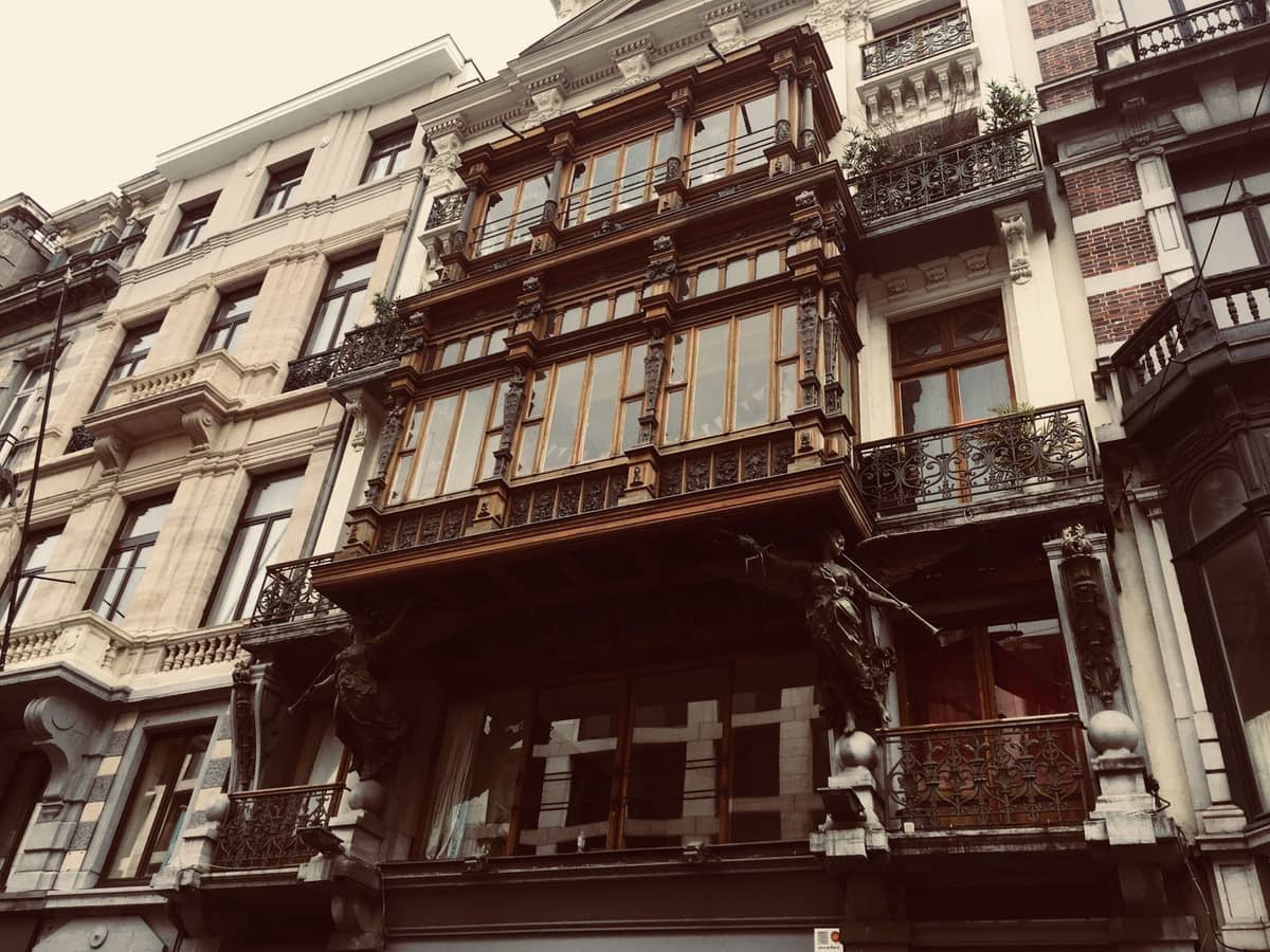 Fachada de um edifício Art Nouveau em Bruxelas com balcões de ferro ornamentados e detalhes decorativos, vista entre dois prédios vizinhos de estilo mais tradicional.