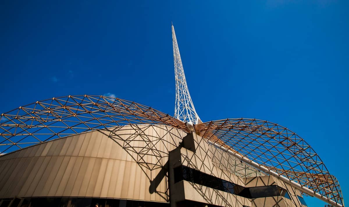Vista gran angular de la icónica aguja y la celosía metálica geométrica del Arts Centre Melbourne bajo un cielo azul intenso.