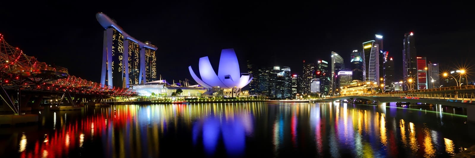 วิวพาโนรามายามค่ำของ Marina Bay พร้อม ArtScience Museum ที่ส่องสว่าง Marina Bay Sands และสกายไลน์ของเมืองสะท้อนลงบนผิวน้ำ