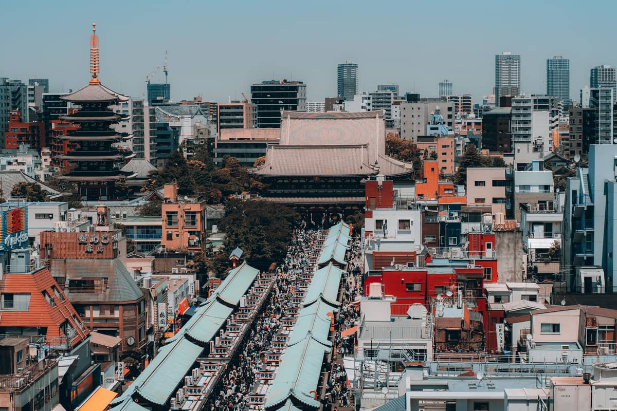 A wide aerial view of Asakusa showing Nakamise shopping street leading to Senso-ji Temple and its five-story pagoda amidst surrounding city buildings.