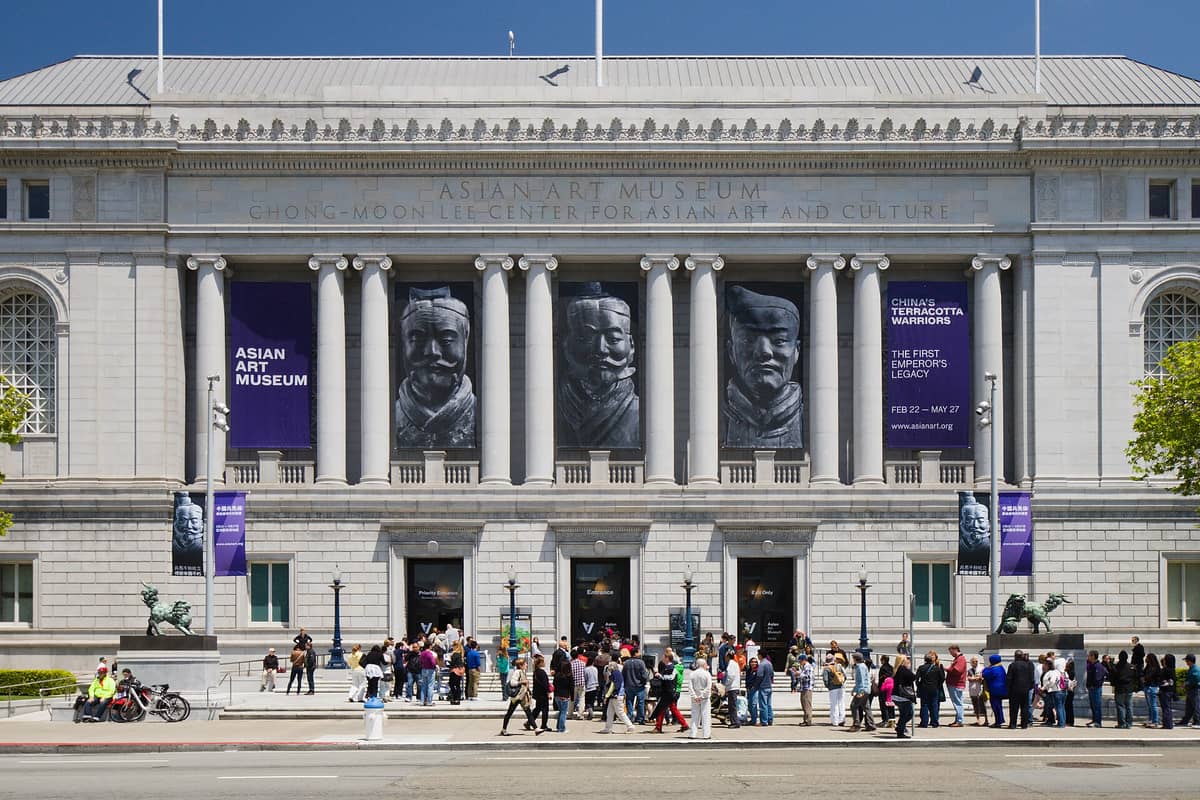 Fachada principal del Museo de Arte Asiático de San Francisco, con visitantes reunidos cerca de la entrada y grandes pancartas anunciando exposiciones.