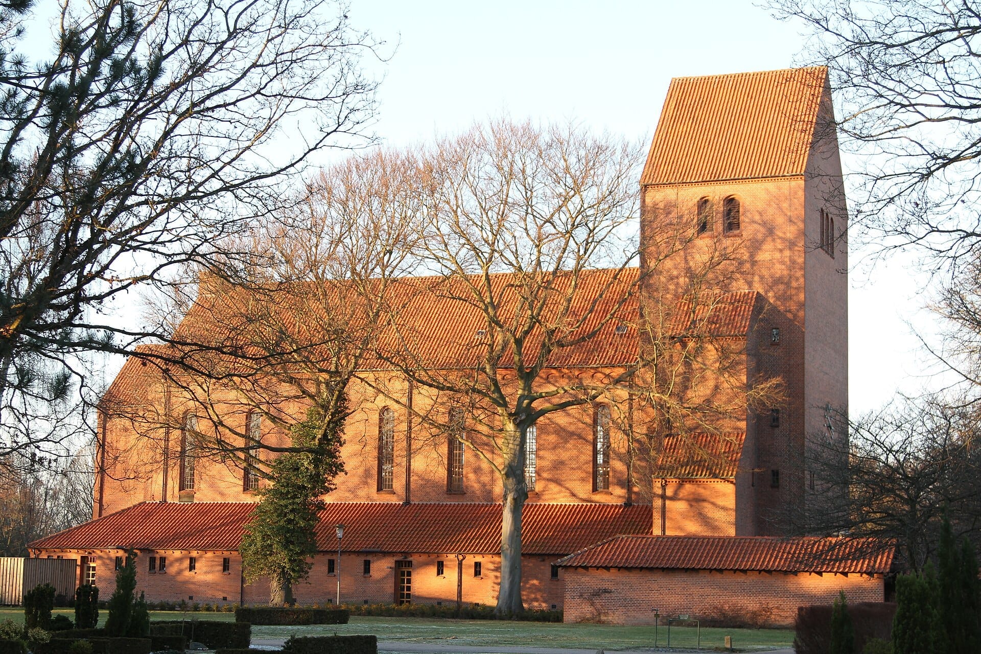 Chiesa in mattoni rossi al cimitero Assistens circondata da alberi spogli nella morbida luce del pomeriggio, Nørrebro, Copenaghen.
