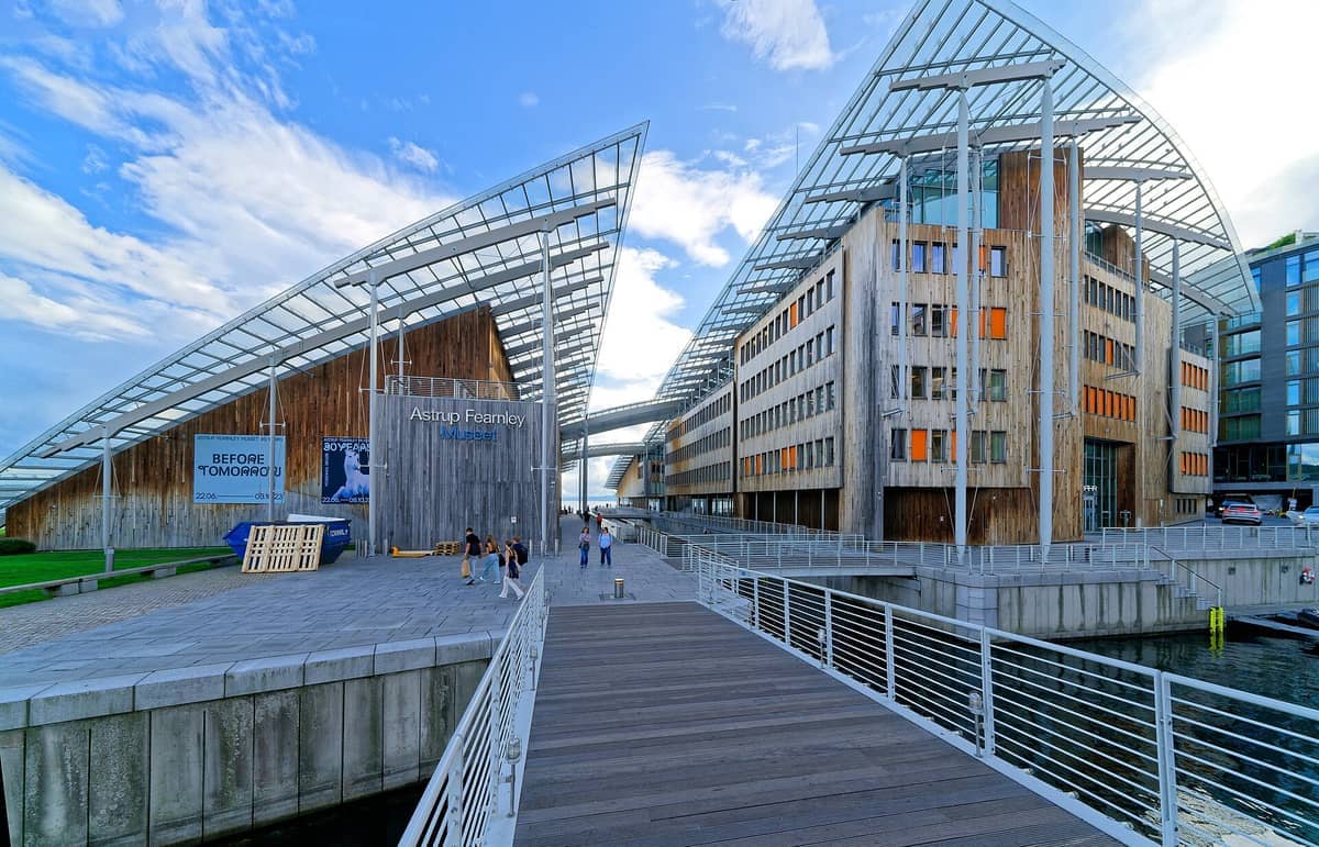 อาคารไม้สมัยใหม่ที่มีหลังคากระจกประกอบเป็น Astrup Fearnley Museum of Modern Art บนริมน้ำของกรุงออสโล พร้อมด้วยผู้เยี่ยมชมที่เดินอยู่ตามทางเดินริมน้ำ
