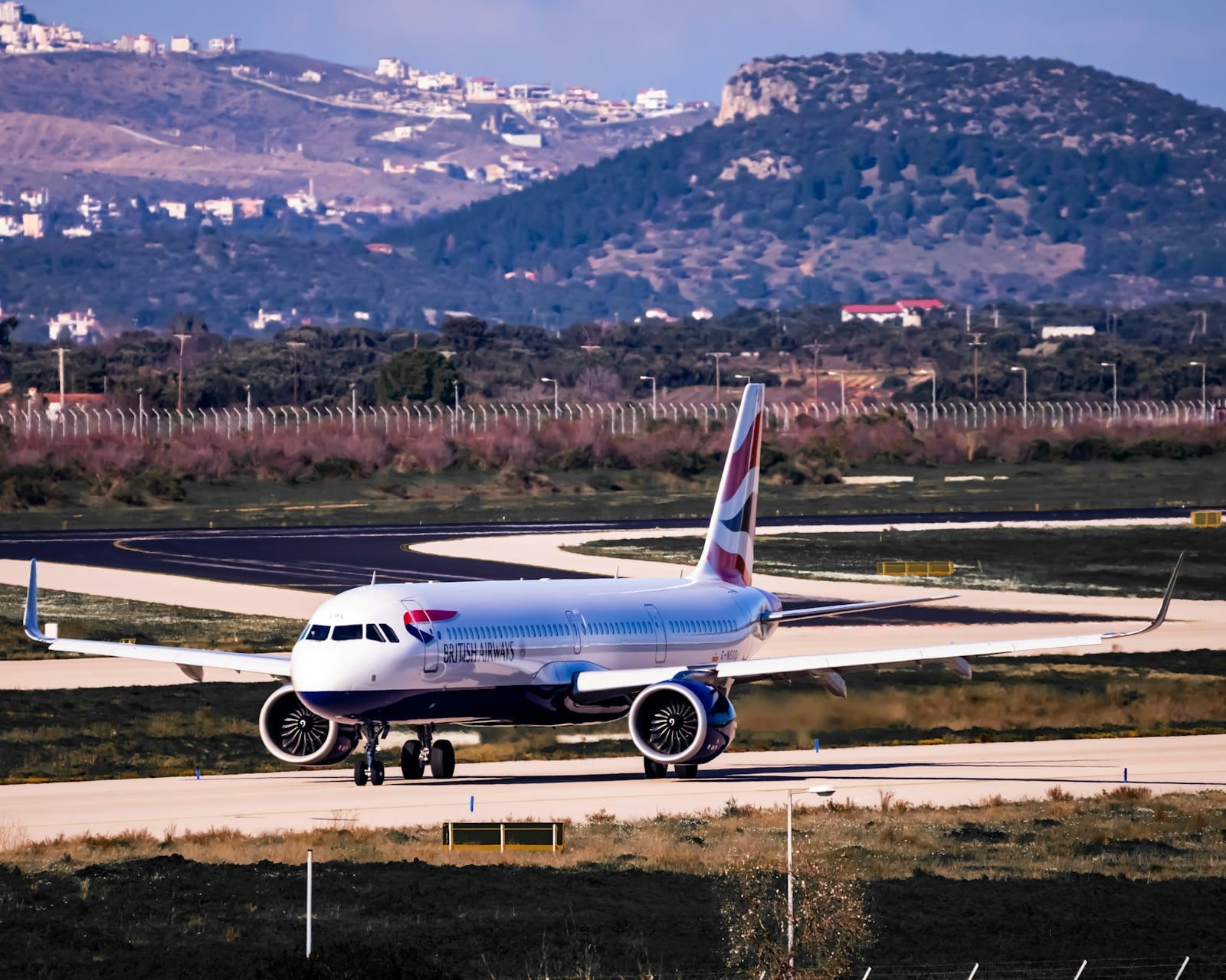 Aereo commerciale che rulla sulla pista dell'Aeroporto Internazionale di Atene, con colline e paesaggio circostante sullo sfondo.