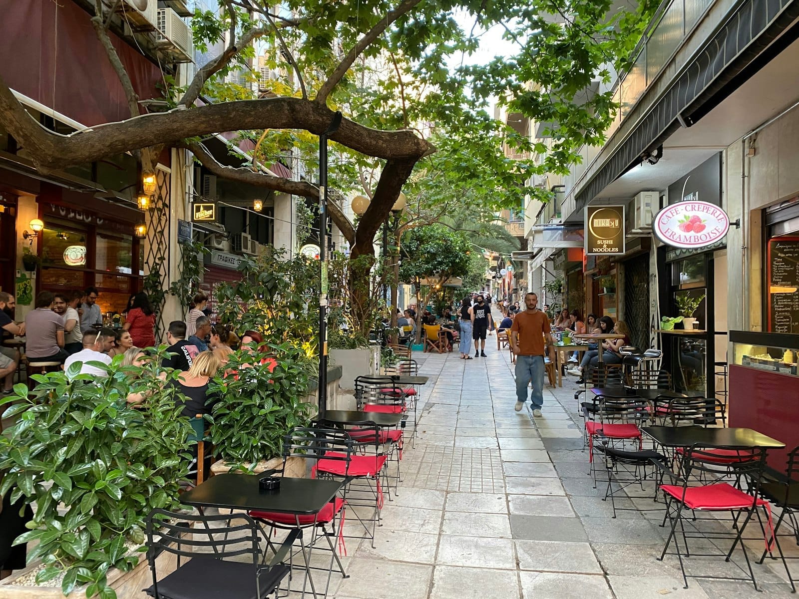 Vivace strada pedonale ad Atene fiancheggiata da caffè sul marciapiede e persone che pranzano, evocando un'atmosfera urbana animata e sicura.