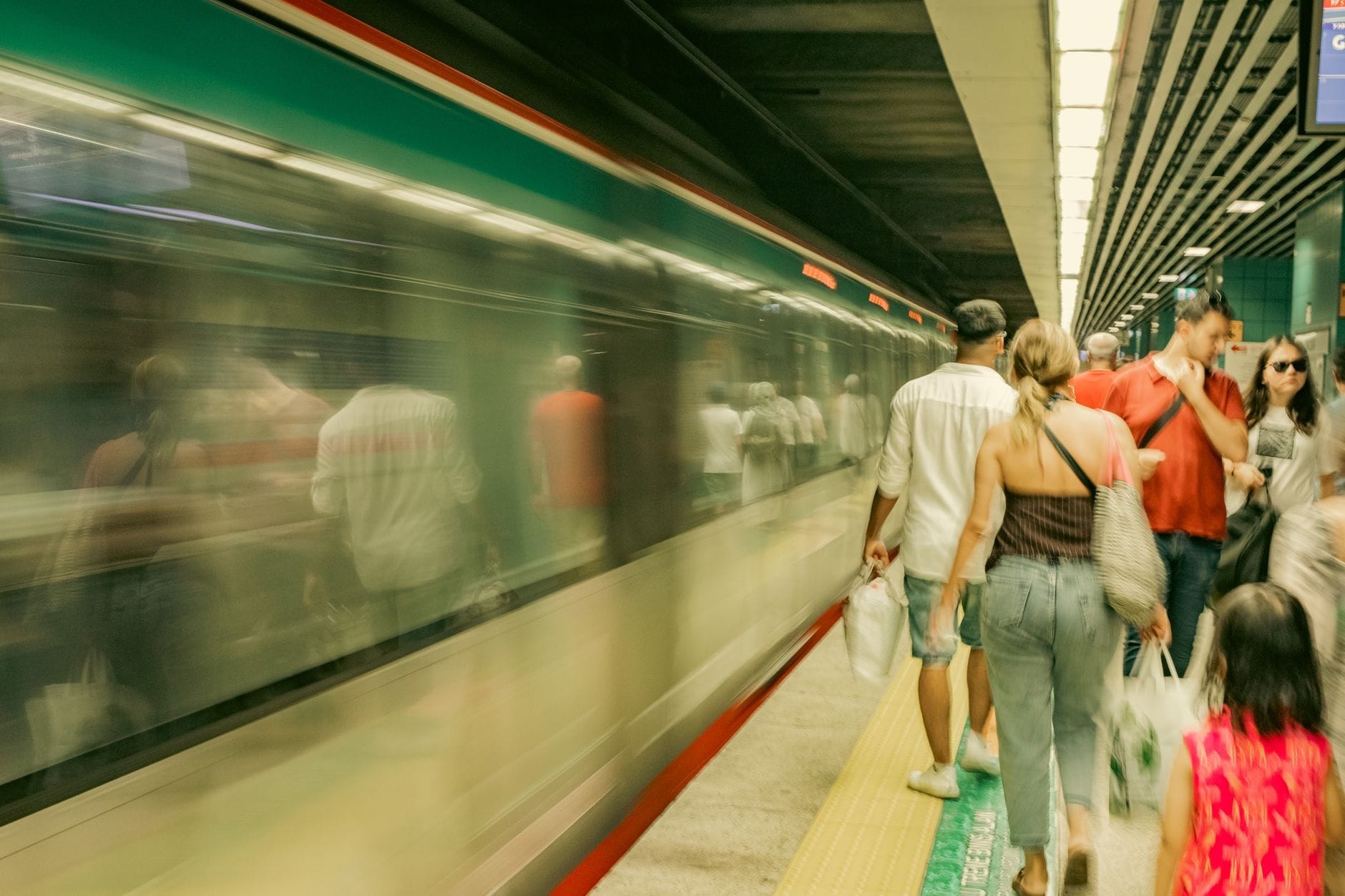Persone in attesa vicino a un treno della metropolitana in movimento su una banchina sotterranea ad Atene, con chiara visibilità del treno e dei passeggeri.