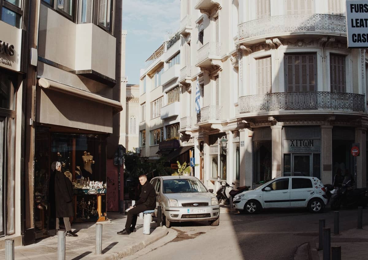 Personas caminando y de compras por una calle de la ciudad con boutiques y arquitectura clásica en Atenas.