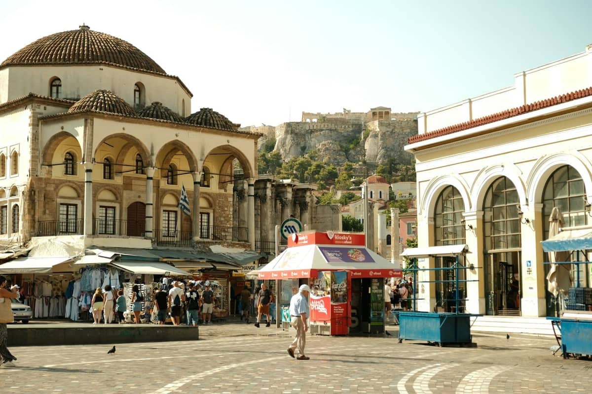 Lebhafter zentraler Platz in Athen mit der Akropolis im Hintergrund und Menschen, die in der Nähe historischer Gebäude spazieren.