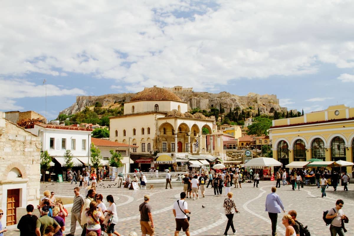 Weitwinkelansicht des Monastiraki-Platzes in Athen mit Spaziergängern, historischen Gebäuden und dem Akropolis-Hügel im Hintergrund