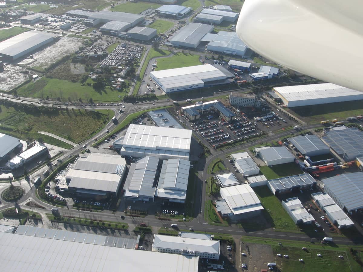 Aerial na tingin ng kumpol ng mga hotel at negosyo malapit sa Auckland Airport, kasama ang mga paradahan at mga paligid na lugar na may halaman.