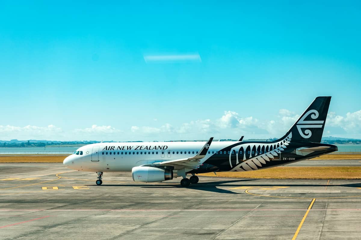 Eroplano ng Air New Zealand na nakaparada sa tarmac ng isang paliparan na may malinaw na langit at malayong tanawin.
