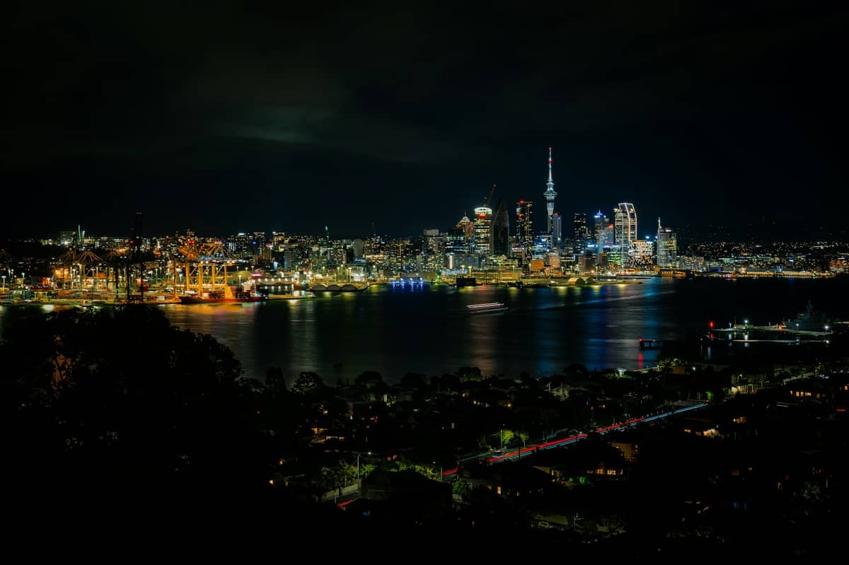 Nocna panorama Auckland z nabrzeżem i podświetloną Sky Tower, widoczna z drugiego brzegu portu.