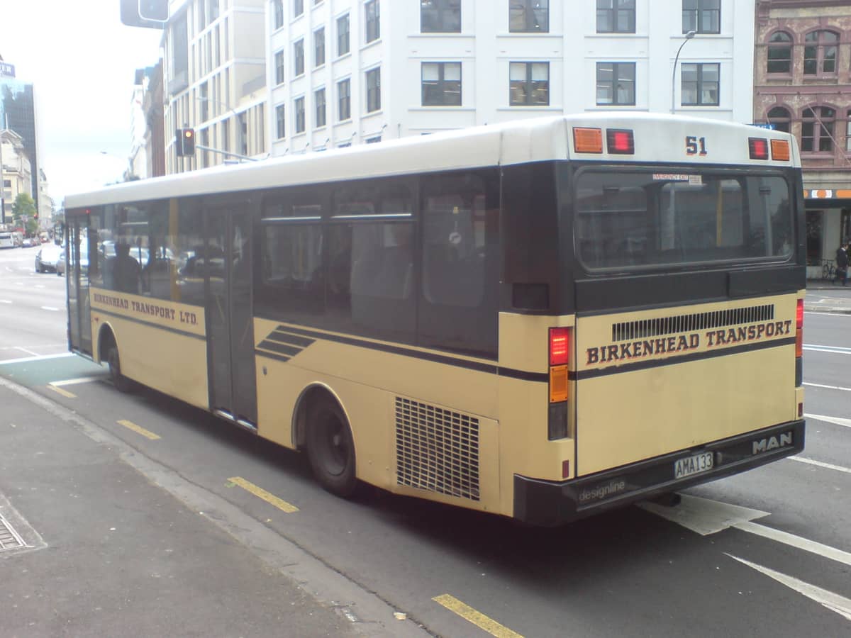 Un bus urbain de Birkenhead Transport dans une rue du centre d'Auckland, avec des immeubles du centre-ville et de la circulation en arrière-plan.